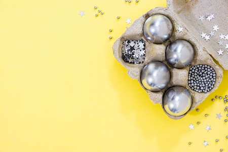 Silver colored Easter eggs and stars in egg box on yellow textured backgroundの写真素材