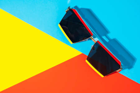 Funky sunglasses on bright yellow, blue and red background with shadow, top view.の写真素材