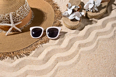 Large round brown summer heat, white sunglasses, sandals and starfish on nice beach sand, top view,...