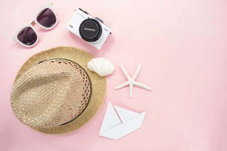 Flat lay traveler accessories on pastel pink background with small white camera, sunglasses, straw...