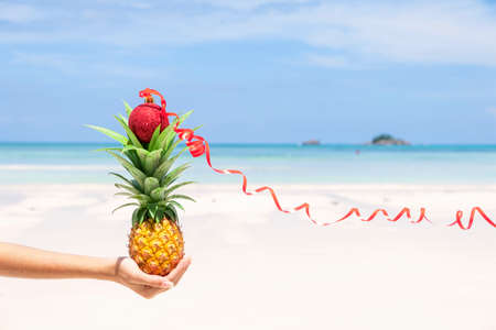 Fresh mini Pineapple on woman hand with single red Christmas ball decoration as a tropical beach Christmas concept.の写真素材