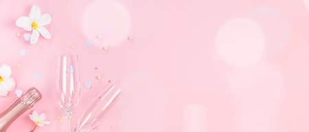 Two empty champagne glasses and bottle of pink champagne with white frangipani flowers and small heart decoration on pink background, copy spaceの写真素材