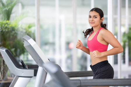 Active young woman running on a treadmill, showcasing the energy and vitality of a healthy...