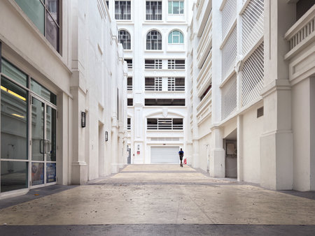 Penang, Malaysia - April 24, 2025: a narrow urban passageway lined with white buildings. A person walks alone toward an entrance. The area appears quiet and well-designed.の写真素材