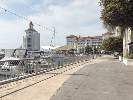 Penang, Malaysia â April 23, 2025: A scenic Straits Quay marina walkway filled with luxury yachts, lined by modern buildings and lush greenery under a clear sky.の写真素材