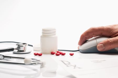 Prescription medicine and pharmacist hand on computer mouse in pharmacy with pill bottles in backgroundの写真素材