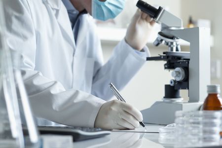 Scientist conducting research taking notes whilst looking through microscope selective focus の写真素材
