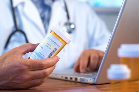 Doctor holding prescription bottle with laptop selective focus