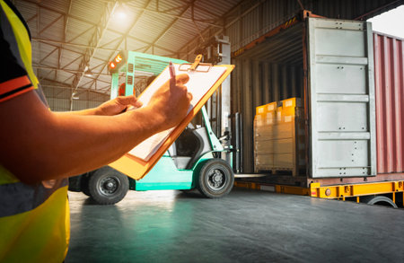 Worker Holds a Clipboard Checking the Loading Cargo Shipment at Distribution Warehouse. Forklift Loading Delivery to Customers. Package Supplies Warehouse. Freight Truck Logisticsの写真素材