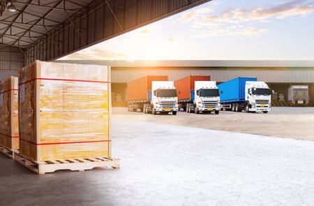 Semi Trailer Trucks on The Parking Lot at Warehouse Port. Bulk of Package Boxes Wrapped Plastic Stacked on Pallets. Distribution Warehouse. Cargo Container Shipping. Freight Truckの写真素材