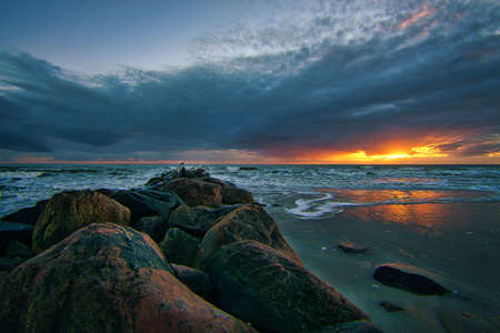 On the beach in BlÃ¥vand, Denmark, with sunset and dramatic clouds. Stones in foreground