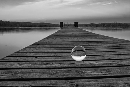 Glass ball on a wooden pier at a Swedish lake at dusk in black and white. Nature shot from Scandinaviaの写真素材