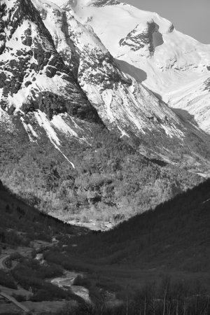 View between mountains in Norway, through which a road leads in black white. Snow on the mountains. Landscape shot from the north in Scandinaviaの写真素材