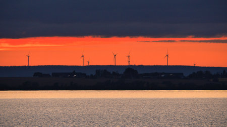 Wind turbine, renewable energy, on a lake at sunset. Clean electricity for climate change. Cloudy sky with orange sunshine in Scandinavia.の写真素材