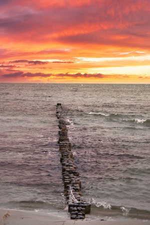 Groynes jut out into the Baltic Sea. Sunset on the horizon. Wooden logs protecting the coast. Landscape from the seaの写真素材