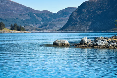 Fjord with mountains on the horizon. Stones reach into the water. The water glistens in the Norwegian sun. Landscape photo from the northの写真素材