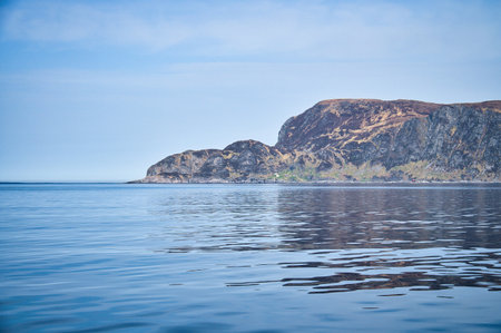 View from the sea to the West Cape in Norway in sunshine. Waves in the foreground, rocks in the...