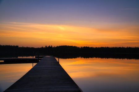 Wooden jetty at sunset on a lake. The colors of the sunset are reflected in the water. A bathing lake in the countrysideの写真素材