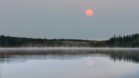 Lake in Sweden, mirror-smooth water, red moon in the sky and trees on the shore. Scandinavian nature in the northの写真素材