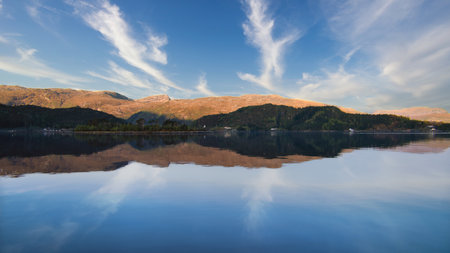 Fjord with view of mountains and fjord landscape in Norway. Blue sky, white clouds, calm mirror-smooth water. Scandinavian landscape shotの写真素材