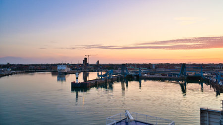 The harbor of Trelleborg, Sweden, at sunrise with calm water, blue harbor facilities and a city view...
