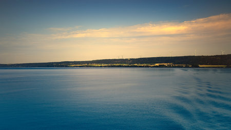 Tranquil seascape under a clear blue sky. The water reflects gentle clouds, while the horizon emphasizes the distance.の写真素材