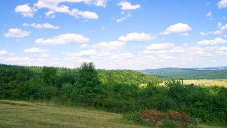 Vast landscape with green forests, rolling hills and a blue sky with white clouds. Idyllic nature, peace and freedom in a summery setting.の写真素材