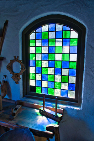 Colorful stained glass window in historical surroundings. Play of light on rustic wooden table with antique tools. Nostalgic atmosphere in vintage styleの写真素材