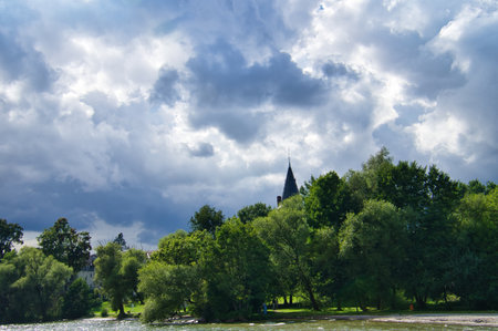 Green river with lush trees, dramatic sky and church tower in the background. Harmonious landscape, ideal for themes such as nature and architecture.の写真素材