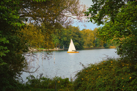 Idyllic lake landscape with sailing boat, framed by green foliage and autumnal trees. Tranquil natural backdrop for relaxation, leisure and enjoyment of nature.の写真素材