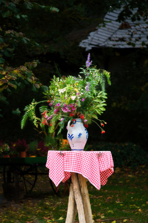 A bouquet of flowers in a vase on a table with a red and white checkered cloth, in the background a garden with trees and plants. Ideal for nature and garden lovers.の写真素材