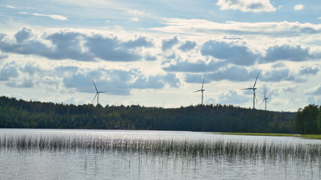 A lake with a reflective surface, wind turbines in the background under a cloudy sky. A combination of nature and sustainable energy in an atmospheric landscape.の写真素材
