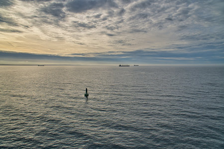 Green buoy in the calm sea at sunrise, ships on the horizon and dramatic sky â maritime morning atmosphere with vastness and quiet power.の写真素材