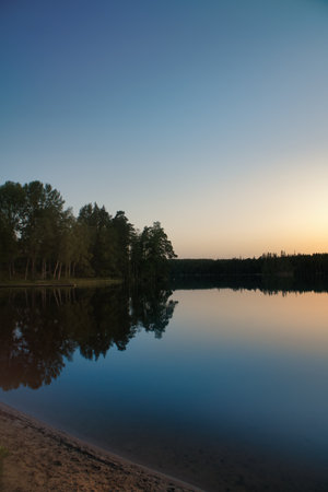 Atmospheric lake in Sweden at sunset, with reflections of the trees. Peaceful landscape, warm colors, and idyllic nature at blue hour.の写真素材