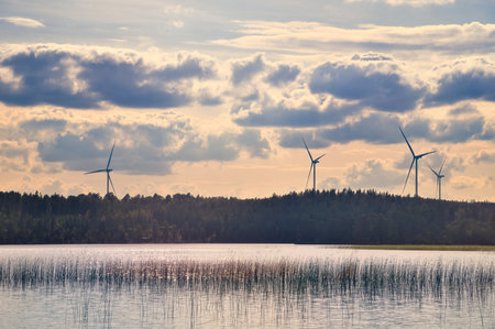 A lake with a reflective surface, wind turbines in the background under a cloudy sky. A combination of nature and sustainable energy in an atmospheric landscape.の写真素材