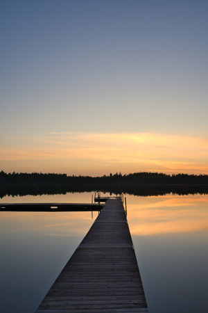 A wooden walkway in Sweden leads into a tranquil lake at sunset. Warm colors, perfect reflections, and a peaceful evening atmosphere in nature.A wooden walkway in Sweden leads into a tranquil lake at sunset. Warm colors, perfect reflections, and a peaceful evening atmosphere in nature.の写真素材