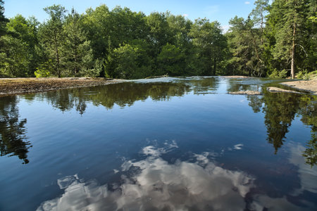 A tranquil lake with clouds and trees reflected in the clear water. A peaceful landscape that exudes...