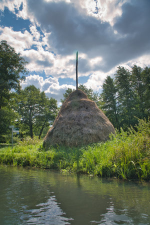 A traditional haystack with a wooden pole amidst lush greenery and under a blue sky. Rural idyll, agriculture, and summer atmosphere.の写真素材