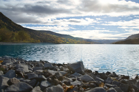 Clear water of a mountain lake with rocks in the foreground, surrounded by autumn-colored hills...