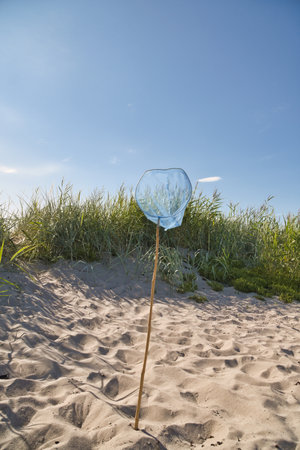 A blue net with a wooden pole on a sandy beach, with a blue sky. A dune with grass behind it. A vacation feeling. A quiet moment in nature, with lightness and structure.の写真素材