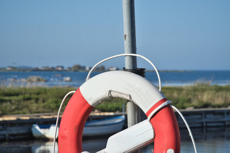 Lifebuoy at a small harbor with a view of water, meadows, and blue sky. A maritime motif with a...