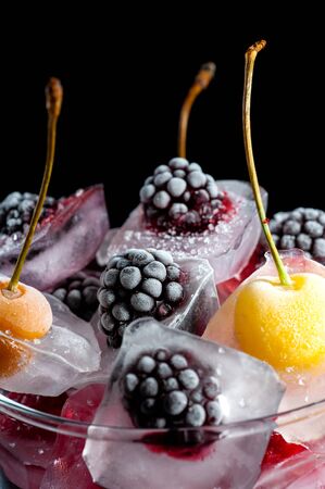  frozen raspberries berries cherries and blackberries in pieces of ice in a glass bowl on a black...
