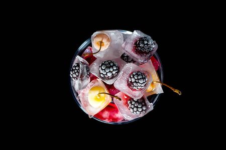  frozen raspberries berries cherries and blackberries in pieces of ice in a glass bowl on a black background.の写真素材