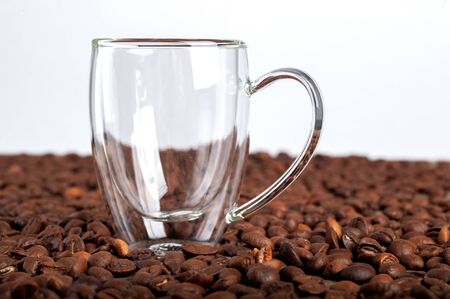 An empty transparent double-bottomed cup stands among coffee beans on a white background. Copyspace.の写真素材