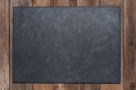 A serving black board made of stone lies on an old wooden background. copyspace.の写真素材