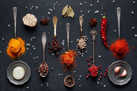 bright colorful multi-colored spices for cooking sprinkled in old spoons on a black background. top shot.の写真素材