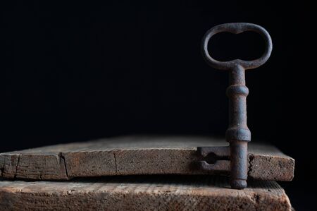 three old rusty keys stand on old wooden board against a dark background.の写真素材
