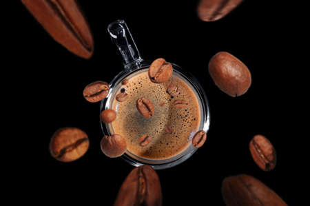 coffee beans fly into a mug with coffee isolated on black background top view