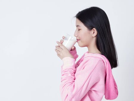 Portrait of healthy teenage girl drinking a glass of milk while standing on white background.