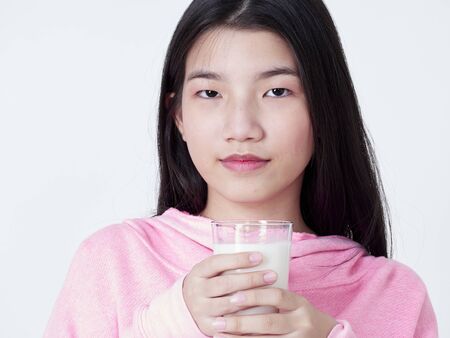 Portrait of cheerful girl with glass of milk while smiling at camera on white background.の写真素材